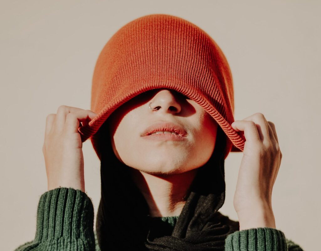 woman pulls an orange hat over her eyes. Representing hiding from anxiety. Emma Schmidt and Associates offer anxiety treatment in Cincinnati and online therapy for anxiety in Ohio and online therapy in Kentucky. 