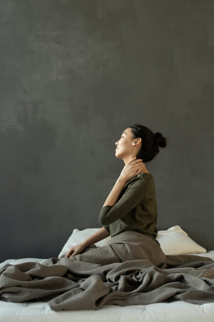 A woman holds the side of her neck while sitting on her bed. This could symbolize the pain that painful intercourse treatment in Indiana can address. Learn more about painful intercourse treatment in Kentucky or painful sex treatment in Cincinnati, OH.