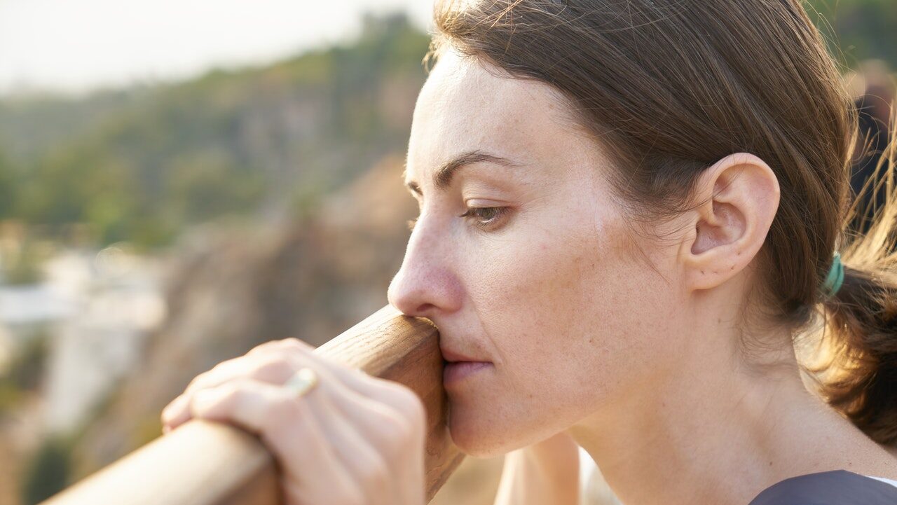 A woman touches her lips and nose against a wooden railing as she looks at the landscape below. She appears tired, with an indifferent stare in her eyes. This could symbolize the emotional numbing that can occur as part of depression symptoms. We offer support with depression treatment in Cincinnati, OH, online depression therapy throughout Ohio, and other services. Contact a depression therapist for the support you deserve.