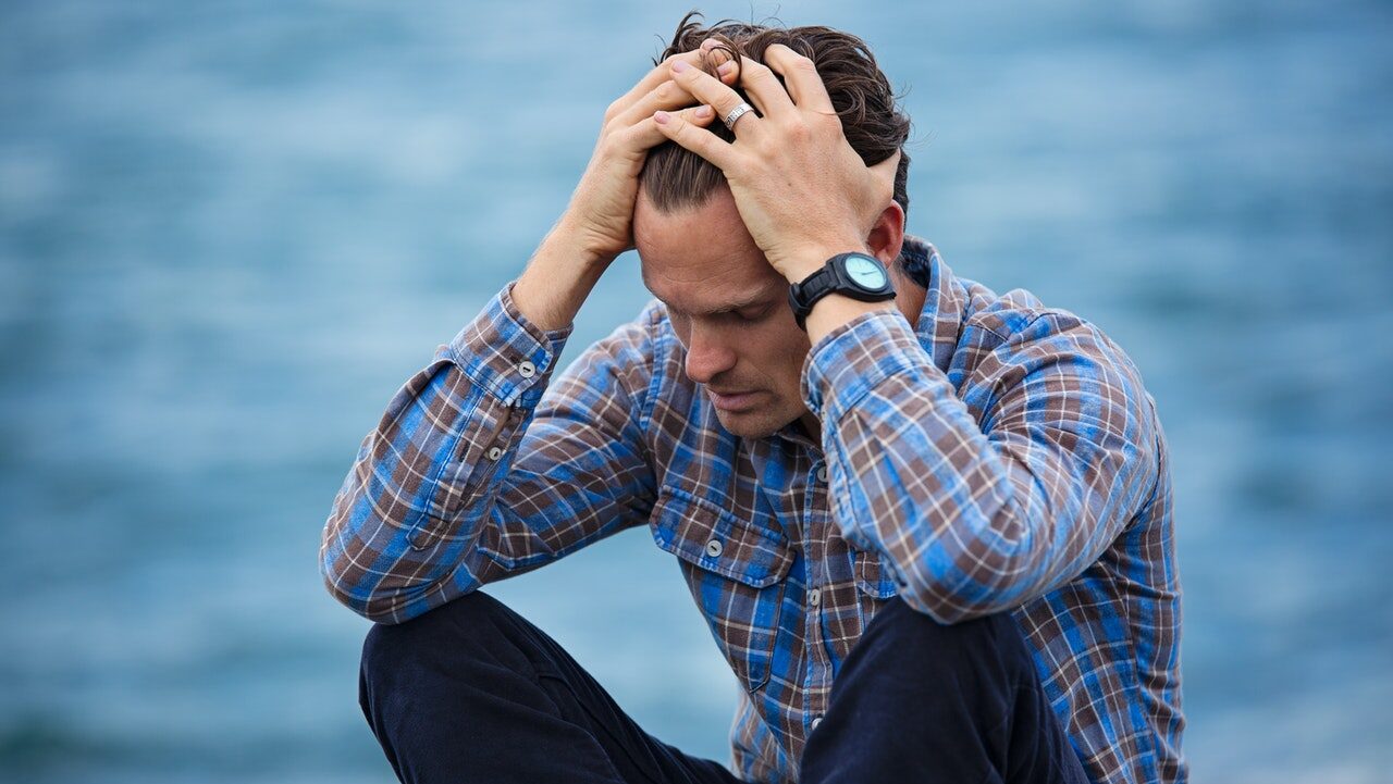 A man sits next to the water while holding his head with both hands. He appears to be experiencing a crisis of some kind, and is in need of support. We offer similar support with depression treatment in Cincinnati, OH. Contact a depression therapist to learn if online depression therapy is right for you!