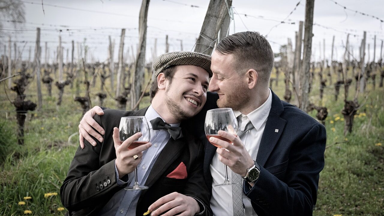 A gay couple embrace at a vineyard while drinking wine. This could represent the need for wine to be intimate with another. Learn about couples counseling in Cincinnati, OH and meet a couples sex therapist for support.  