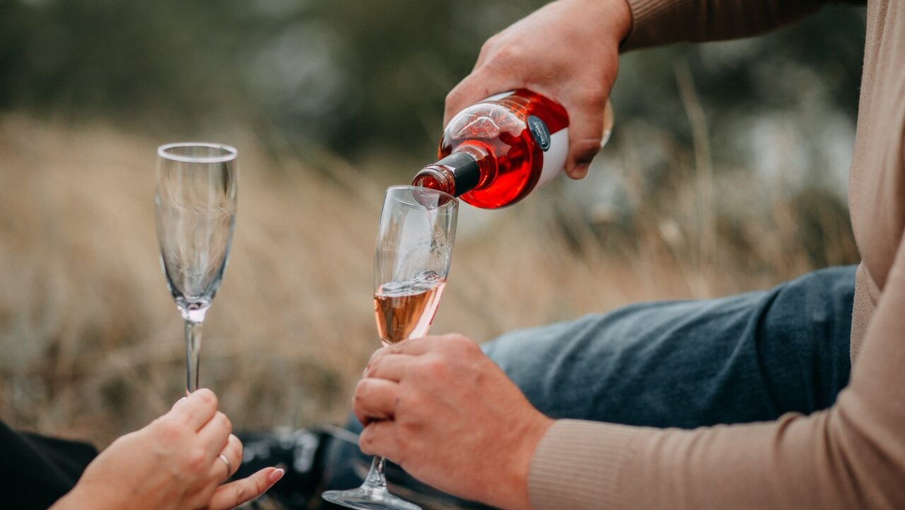 A person pours wine into a glass as their partner holds out their own glass. This could symbolize a couple that could benefit from searching for  "couples sex therapist near me" to overcome alcohol dependency. Contact us to learn more about sex therapy in Cincinnati, OH and other services.
